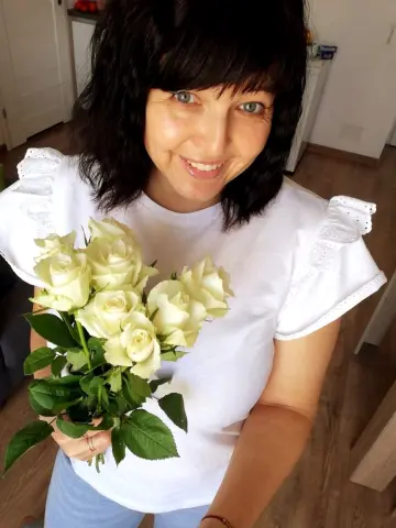 Polunichka039 smiles at the camera while holding a large bouquet of white roses and wearing a white t-shirt.
