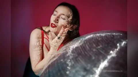 Woman in a red dress with eyes closed, featuring artistic light patterns in a moody, cinematic setting.