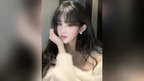 Young woman with long dark hair wearing a white fuzzy sweater in a soft, dreamy indoor setting.