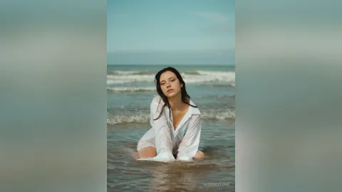 MiaAngelove — MiaAngelove sits in the ocean waves wearing a wet, white button-down shirt.