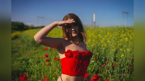 Young woman in a red strapless top posing in a sunny yellow flower field under a clear blue sky.