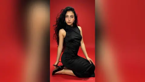 Elegant woman in a sleek black satin dress posing against a vibrant red background with a sophisticated mood.