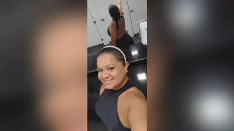 Smiling woman in a black sleeveless top and headband posing for a selfie in a modern restroom.