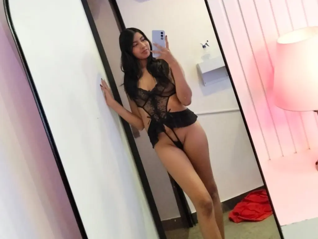 lannadoll22 sucks on a large tan dildo while wearing a black lace top with pink bows in her hair.