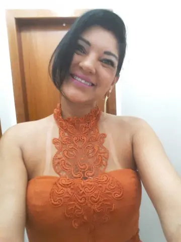 Smiling woman in an elegant burnt orange lace halter dress posing indoors for a portrait.