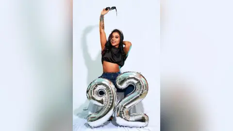 Smiling woman in a black crop top celebrating her 92nd birthday with large silver number balloons.