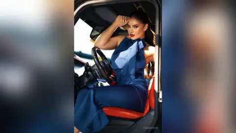 Elegant woman in a blue sleeveless jumpsuit sitting inside a luxury car with a sophisticated mood.