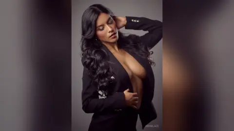 AriaBlaze poses in a black blazer, showing off her large breasts and long wavy dark hair against a plain background.
