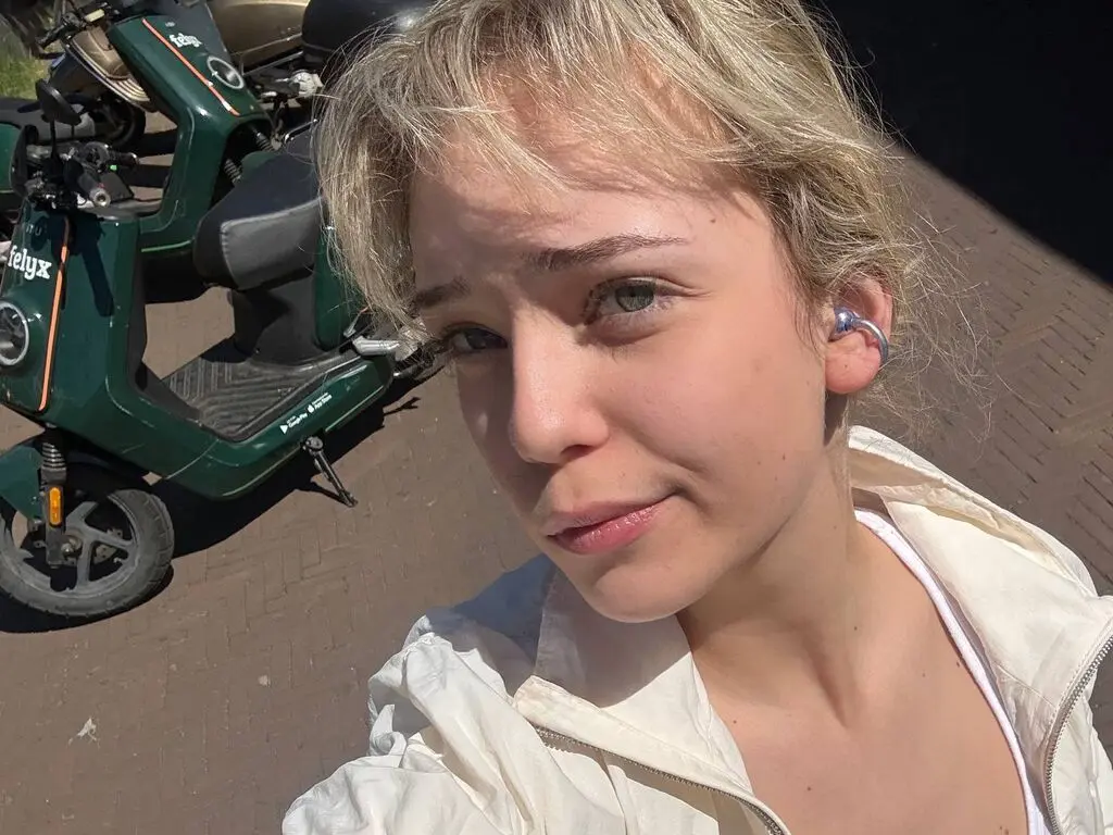 KeilaTouchton takes a sunny outdoor selfie wearing a white jacket and a white top.