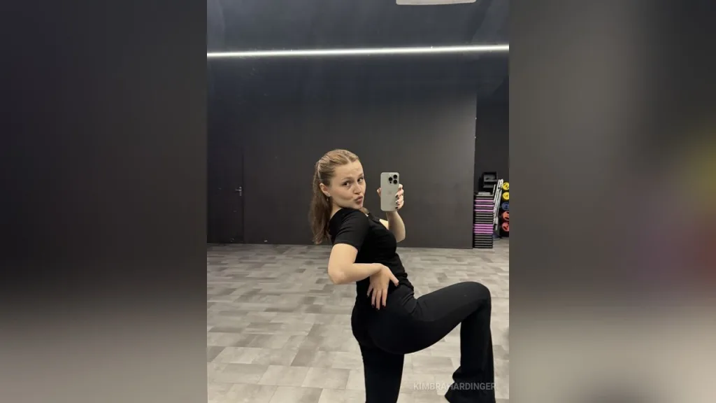 Blonde woman in a black t-shirt posing with a relaxed expression in a bright indoor setting.