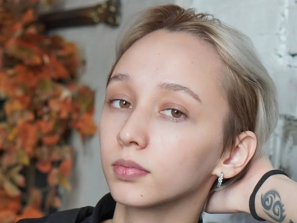 Close-up portrait of a blonde woman with natural makeup and silver earrings in a soft, moody indoor setting.