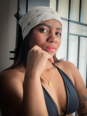 Charlotte_fuentes wearing a white bandana and black bikini top, posing with her hand under her chin.