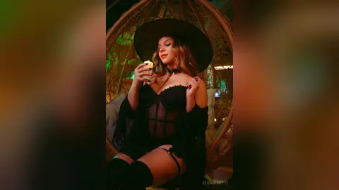 Glamorous woman in black lingerie and lace robe relaxing in a wicker egg chair at night.