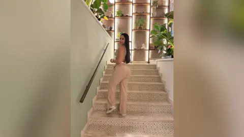 Stylish woman in beige linen trousers and tank top posing on elegant patterned stairs in a modern home.
