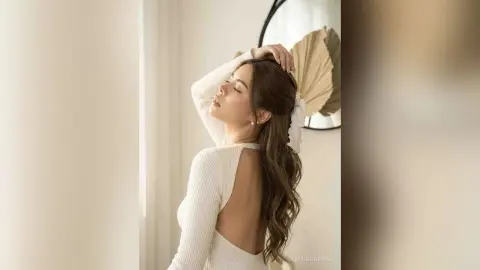 JasminAndres poses with her eyes closed and hand in her hair, wearing a white long-sleeved backless top.