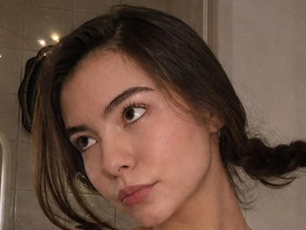 Young woman with brown hair and natural makeup looking away in a warm, indoor setting.