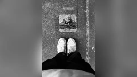 Top down view of white sneakers and black trousers standing on a Coyoacán street tile in black and white.