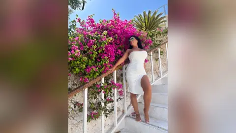 MissyJolie poses on white stairs wearing a white strapless dress next to bright pink bougainvillea flowers.