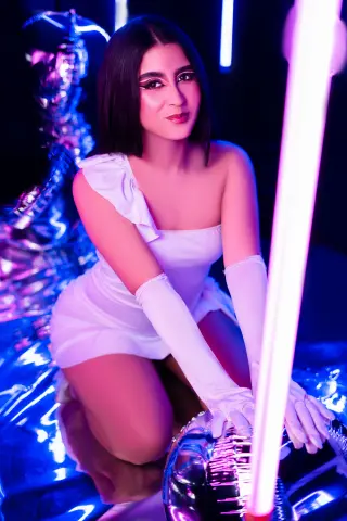 Elegant woman in a white cocktail dress and long gloves posing amidst glowing neon lights in a dreamy mood.