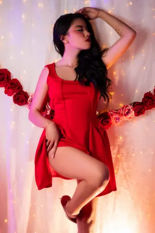 Young woman in a red cocktail dress posing against a dreamy backdrop of fairy lights and soft fabric.