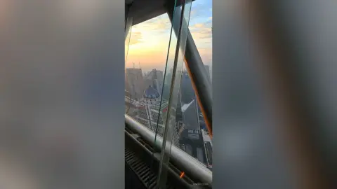 Panoramic cityscape view of urban skyscrapers during a golden sunset from a high-rise glass balcony.