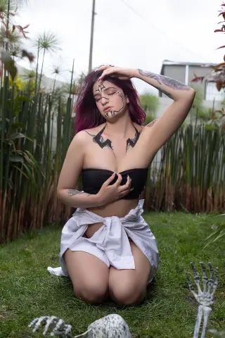 Woman in black tube top and white skirt posing with skeleton props in a lush green garden.
