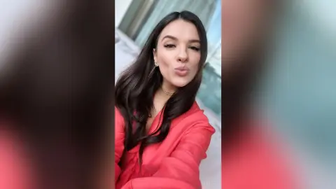 Rebecca pouts her lips at the camera while wearing a red top and gold necklace.