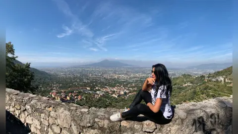 MissyJolie sits on a stone wall overlooking a vast valley and distant mountains under a clear blue sky.
