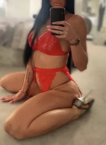 Woman in red lace lingerie set sitting on a floor for a sensual indoor mirror selfie.