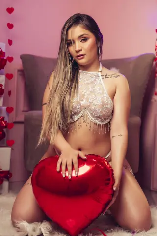 Young woman in white lace lingerie holding a red heart balloon in a romantic, dreamy setting.