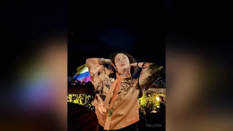 Cheerful woman in a patterned silk blouse posing outdoors at night under a dark sky.
