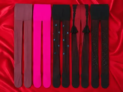 A collection of five pairs of colorful tights, including pink, black, and patterned styles, laid out on a red satin fabric background.