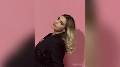 Elegant woman in a black blazer posing against a pink background with a sophisticated mood.