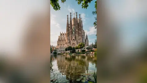 Majestic Sagrada Familia cathedral reflecting in a peaceful lake under a clear blue sky in Barcelona.