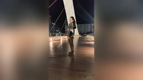 Stylish woman in a black crop top and shorts posing on a wooden city boardwalk at night under urban lights.
