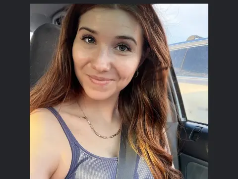 Smiling young woman with long reddish-brown hair wearing a blue tank top sitting in a car seat.