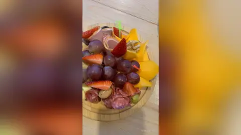 Gourmet charcuterie board featuring fresh strawberries, red grapes, sliced meats, and cheese on a wooden platter.