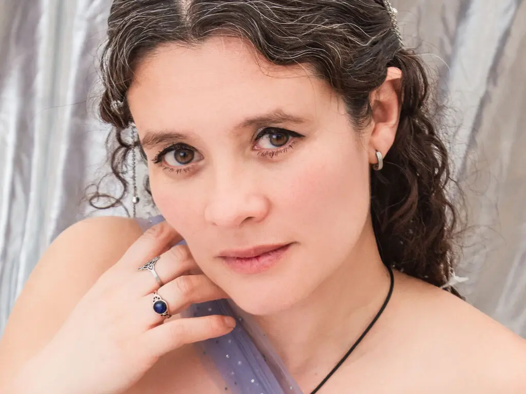 Close-up portrait of a woman with curly hair and silver rings in a soft, dreamy setting.