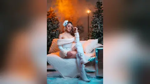 Elegant woman in white winter outfit sitting on a sofa in a cozy, dreamy holiday setting.
