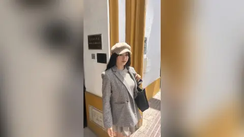 Stylish woman in a grey plaid blazer and beige cap posing in front of a white building entrance.