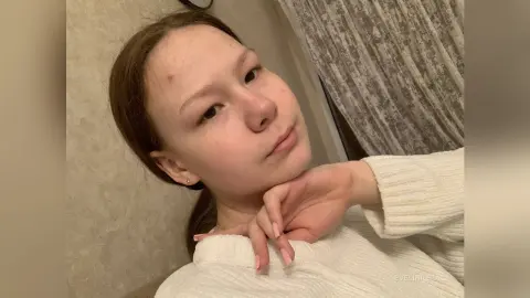 Young woman in a cozy white knit sweater posing with a thoughtful expression in a warm indoor setting.