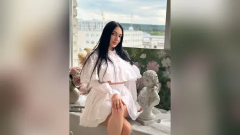 TessaWinsent — TessaWinsent sits by a window wearing a white ruffled crop top and matching skirt.