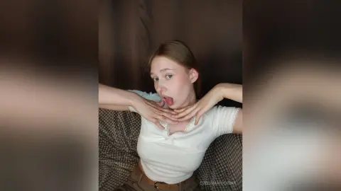 Young woman in a white lace blouse posing playfully in a cozy indoor setting.