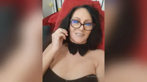 Smiling woman with glasses and black bow accessory relaxing in a cozy red setting.