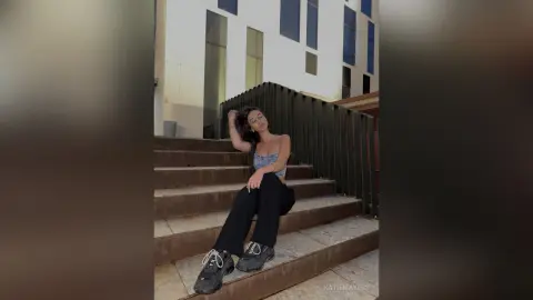 Young woman in a blue tube top and black trousers sitting on outdoor stairs with a relaxed, casual mood.