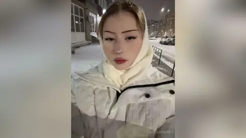 Young woman in a white winter puffer jacket and cream scarf posing on a snowy city street at night.