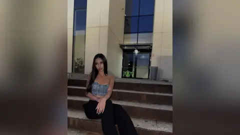 Young woman in a denim corset and black trousers sitting on outdoor stairs at night with a moody aesthetic.
