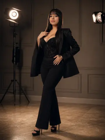 Elegant woman in a black blazer and lace bodysuit posing in a professional photo studio setting.