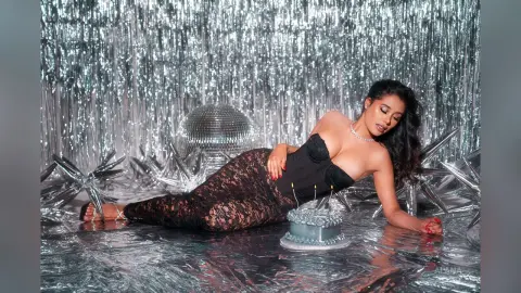 Glamorous woman in a black lace dress reclining against a disco ball in a silver sparkly party setting.