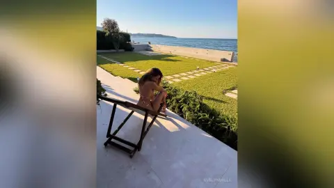 EvelynMills sits on a wooden bench outdoors, wearing a tiny tan bikini and looking down while exposing her bare breasts and pussy.